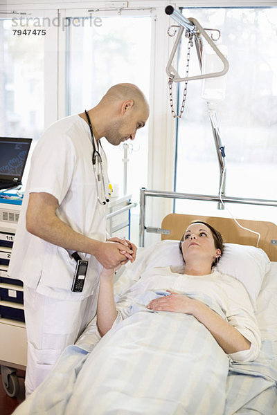 Männlicher Arzt tröstliche Patientin auf dem Bett in der Krankenstation