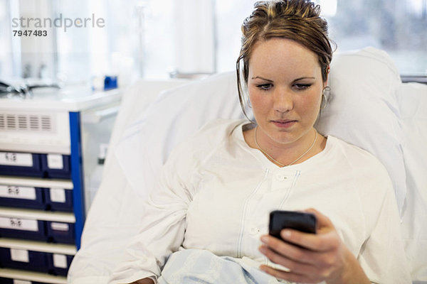 Mittlere erwachsene Patientin  die das Handy benutzt  während sie auf dem Bett in der Krankenstation liegt.