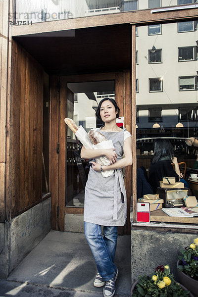 Porträt einer selbstbewussten jungen Besitzerin mit Brotlaibchen vor der Bäckerei