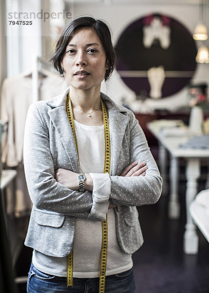 Porträt einer selbstbewussten Modedesignerin mit gekreuzten Armen im Atelier