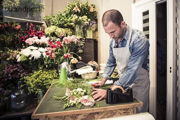 Mittlerer erwachsener männlicher Florist mit Blumenstrauß am Schreibtisch im Geschäft