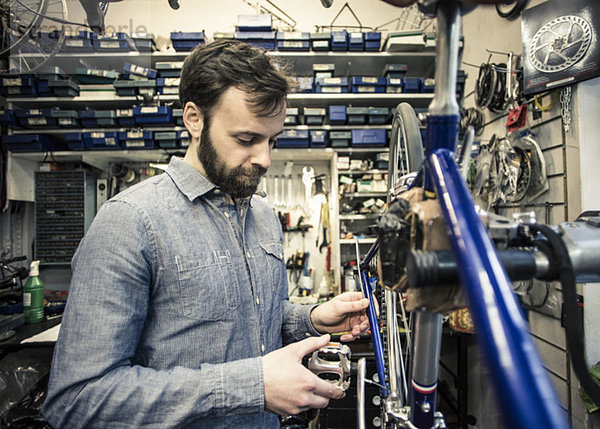 Mittlerer erwachsener Monteur  der das Fahrrad in der Werkstatt repariert.