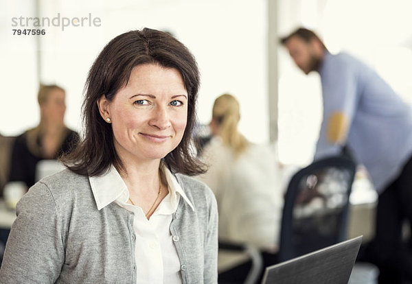 Porträt einer mittleren erwachsenen Frau mit Kollegen im Hintergrund im Büro