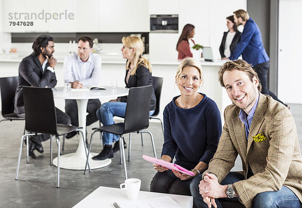 Portrait von glücklichen Geschäftsleuten mit Kollegen  die im Hintergrund im Bürorestaurant diskutieren.