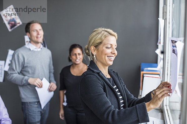 Mittlere erwachsene Geschäftsfrau klebt Papier mit Kollegen im Hintergrund im Büro