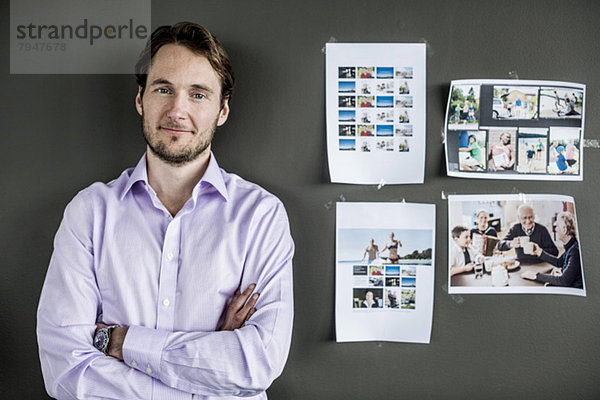 Porträt eines mittelgroßen Geschäftsmannes  der im Büro an der Wand steht.