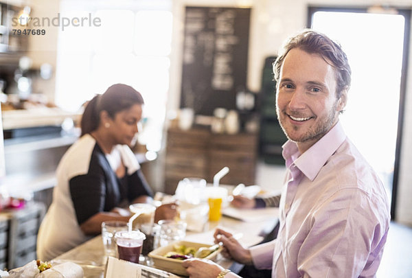 Seitenansicht Porträt eines mittelgroßen Geschäftsmannes beim Frühstück mit Kollegen im Hintergrund im Bürorestaurant