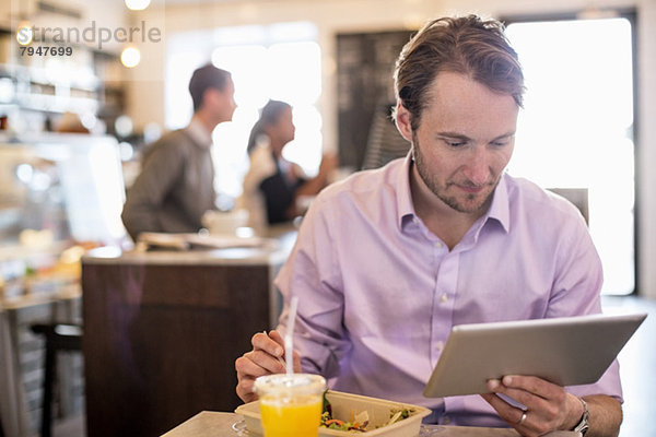 Mittlerer erwachsener Geschäftsmann  der sich beim Frühstück am Tisch im Restaurant ein digitales Tablett ansieht.