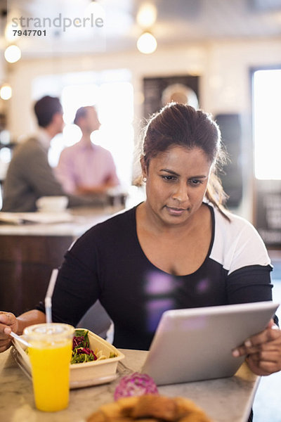 Geschäftsfrau mit digitalem Tablett beim Frühstück am Restauranttisch mit Kollegen im Hintergrund