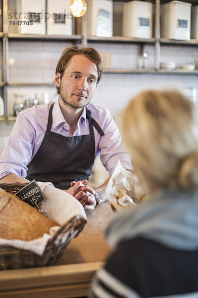 Mittlerer erwachsener männlicher Besitzer mit Blick auf weibliche Kundin im Restaurant