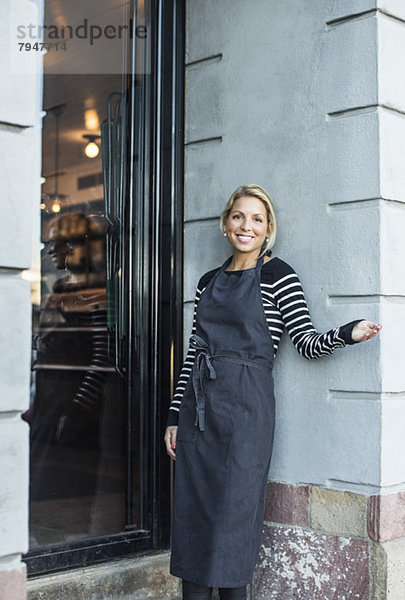 Mittlere erwachsene Besitzerin gestikuliert  während sie sich an der Wand vor dem Restaurant lehnt.