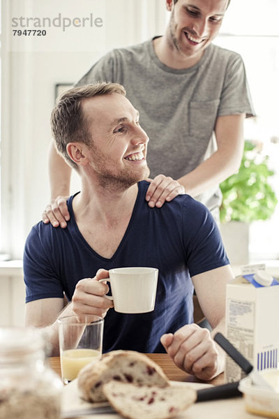 Junger schwuler Mann massiert Partner beim Frühstück am Tisch