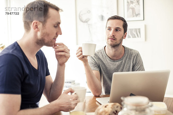 Homosexuelles Paar beim Frühstück mit Laptop am Tisch zu Hause
