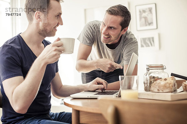 Homosexuelles Paar mit Laptop zusammen am Frühstückstisch zu Hause