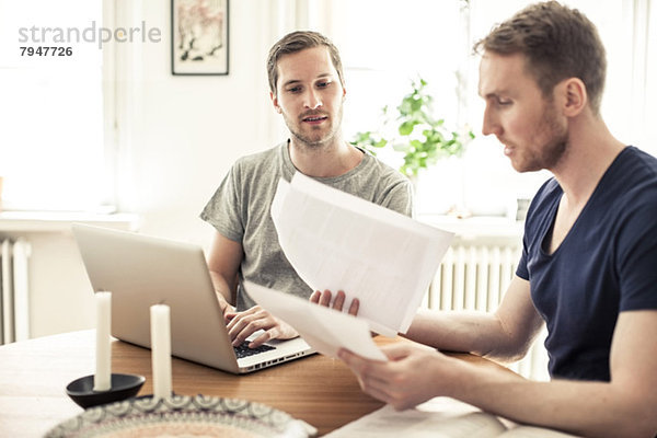 Homosexuell Mann Lesung Papier während Partner mit Laptop am Tisch zu Hause