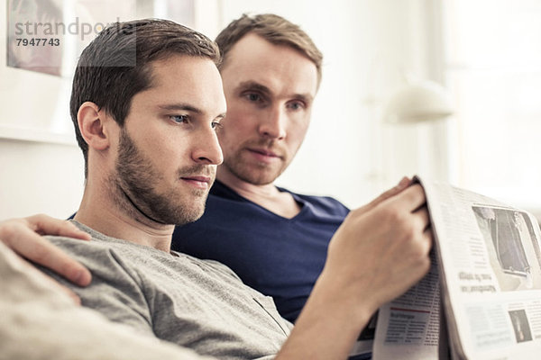 Homosexuelles Paar beim gemeinsamen Zeitungslesen zu Hause
