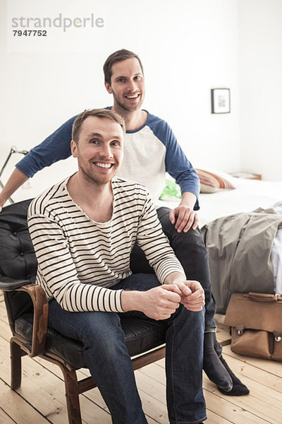 Porträt eines glücklichen homosexuellen Paares  das auf einem Stuhl im Schlafzimmer sitzt.