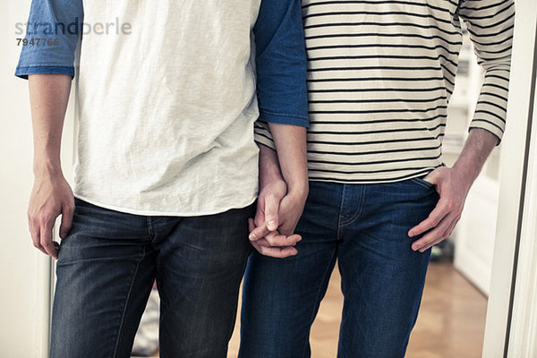 Vorderansicht Mittelteil eines jungen homosexuellen Paares  das zu Hause Händchen hält.