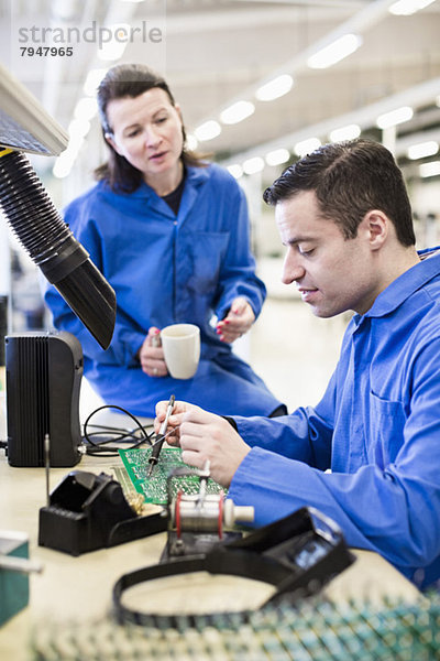 Elektrikerlötleiterplatte mit Kollegen auf dem Schreibtisch in der Industrie