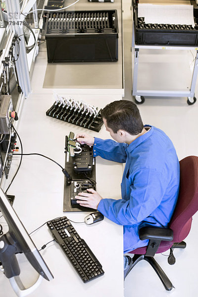 Hochwinkelansicht eines reifen Elektrikers  der an einem Maschinenteil am Schreibtisch in der Industrie arbeitet.