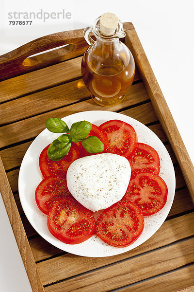 Büffelmozzarella mit Basilikum  Tomaten und einer Flasche Olivenöl auf dem Teller  Nahaufnahme