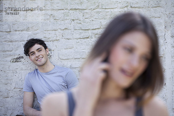 Junge Frau spricht auf dem Handy  während Mann im Hintergrund