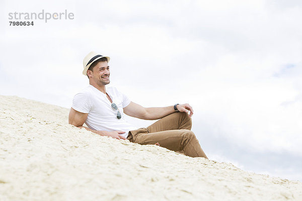 Porträt eines jungen Mannes auf Sand liegend  lächelnd