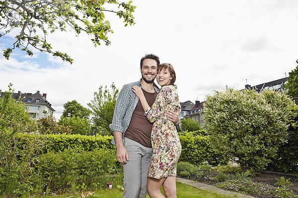 Deutschland  Köln  Junges Paar  das sich im Garten umarmt  lächelnd
