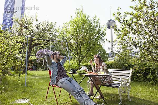 Deutschland  Köln  Junges Paar beim Frühstück im Garten  lächelnd