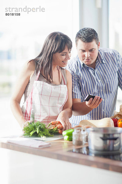 Paar  das während der Zubereitung des Essens auf das Smartphone schaut