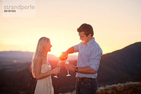 Junges Paar bei Sonnenuntergang im Freien mit Champagner