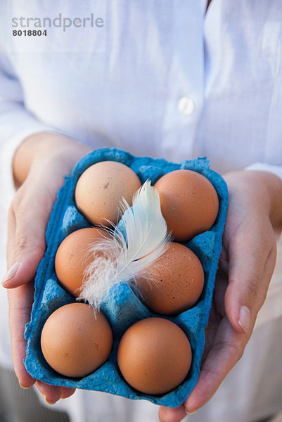 Frau hält sechs Eier in der Schachtel mit Feder