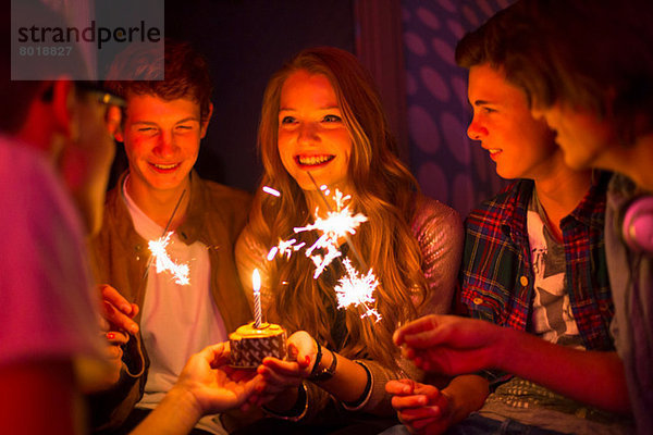 Gruppe von Teenagern sitzend um Geburtstagskuchen mit Wunderkerzen