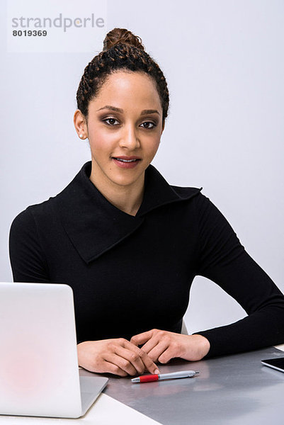 Portrait einer jungen Frau am Schreibtisch mit Laptop