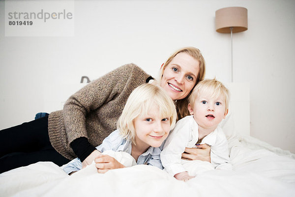Porträt von Mutter und zwei kleinen Söhnen auf dem Bett liegend