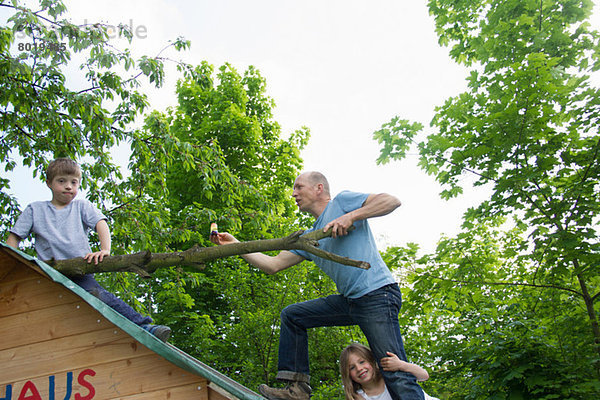 Vater und zwei Kinder klettern auf das Spielhausdach