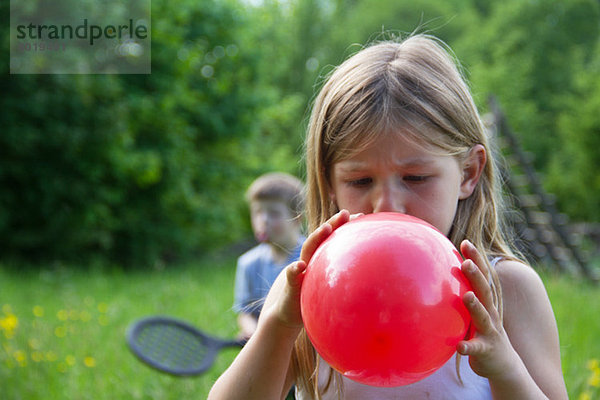 Nahes Porträt des jungen Mädchens beim Aufblasen des roten Ballons