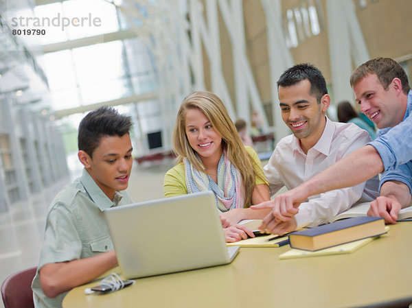 Junger Mann und Studieren mit Tutoren  die auf den Laptop zeigen.