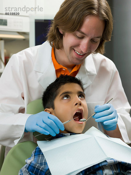 Zahnarzt schaut in den Mund des Jungen