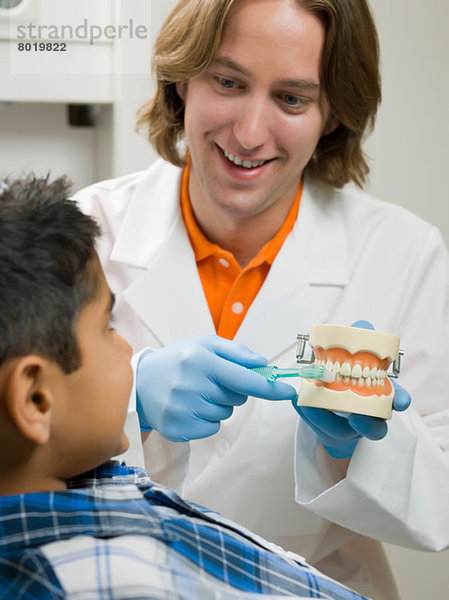 Zahnarzt zeigt dem kleinen Jungen  wie man die Zähne am Modell putzt.