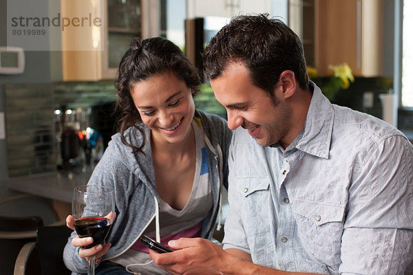 Junges Paar mit Weinglas und Blick aufs Handy