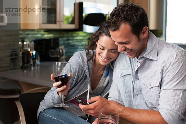 Junges Paar mit Weinglas und Blick aufs Handy