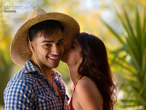Junge Frau küssend Mann mit Sonnenhut  lächelnd