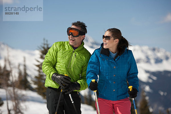 Junge Frau und reifer Mann in Skibekleidung mit Skistöcken