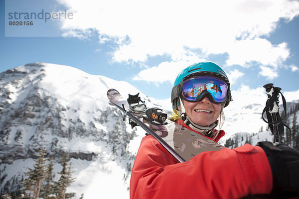 Junge Frau in Skibekleidung hält Skier über die Schulter  lächelnd