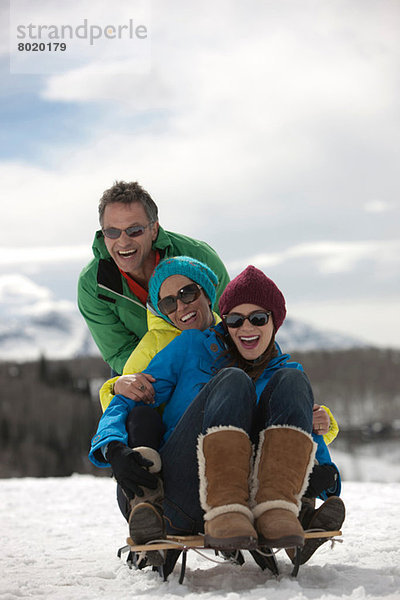 Drei Freunde sitzen auf einem Schlitten im Schnee.