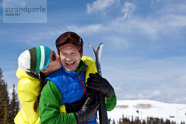 Junge Frau in Skibekleidung küssend reifer Mann mit Skiern