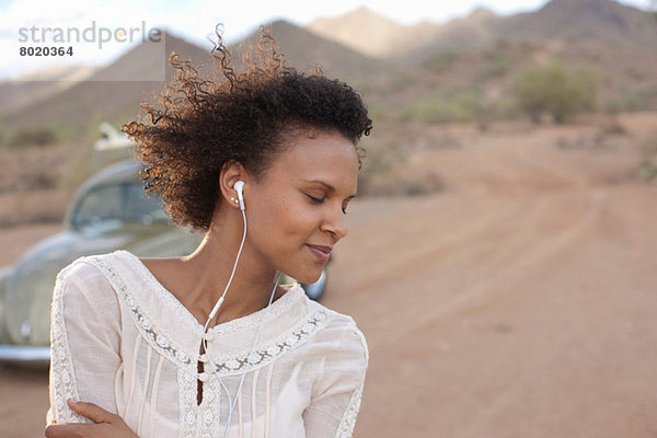 Junge Frau mit Kopfhörern in der Wüste auf Roadtrip  lächelnd