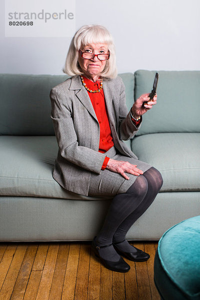 Seniorin auf dem Sofa sitzend  Handy haltend