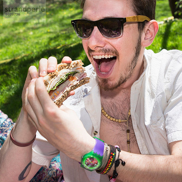 Mann mit Sonnenbrille isst Sandwich